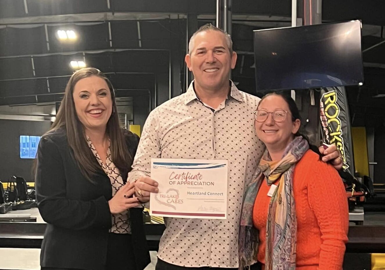 Three business professionals posing with a certificate in front of a gym.