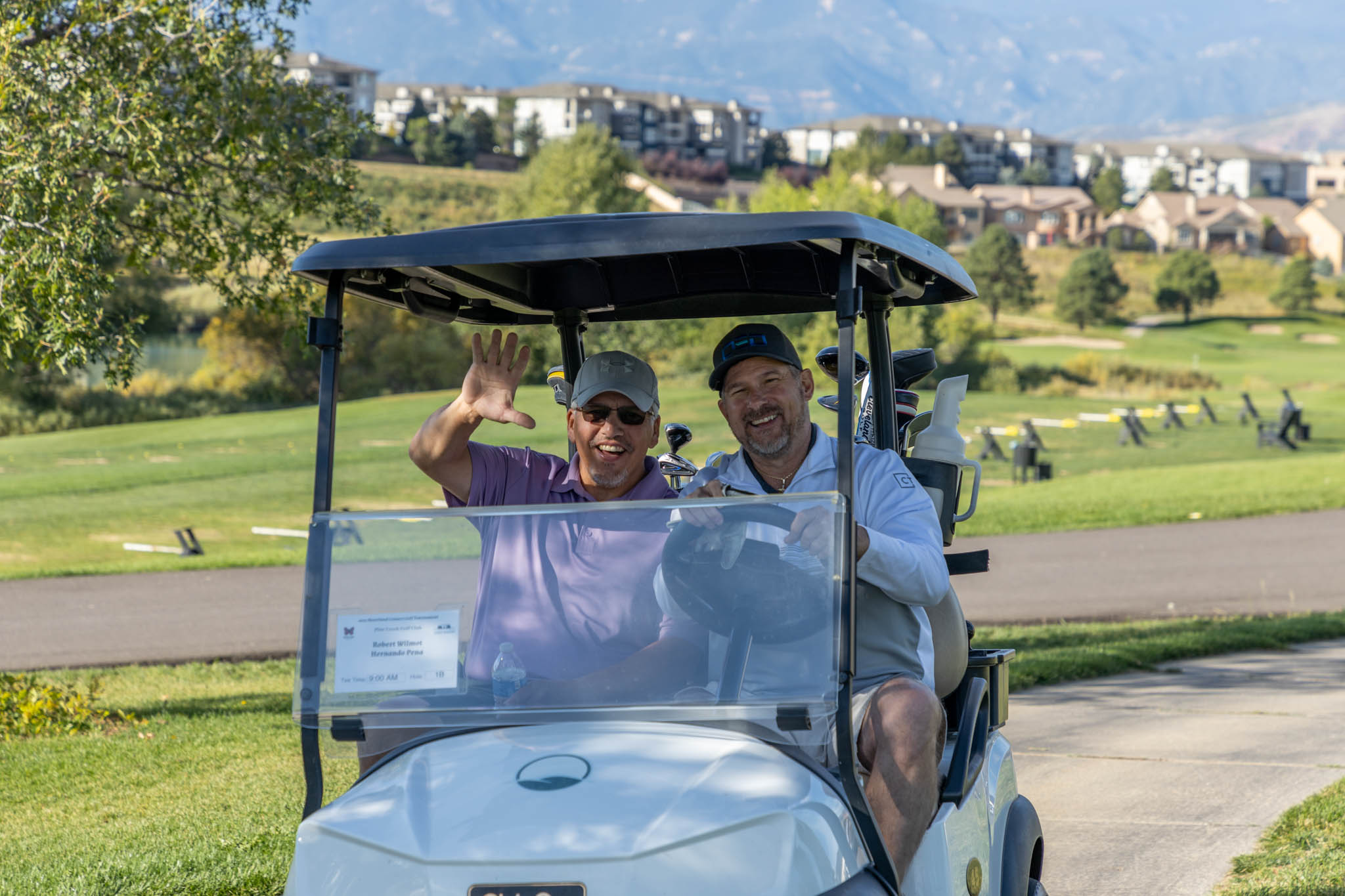 Two men riding in a golf cart with mountains in the background.